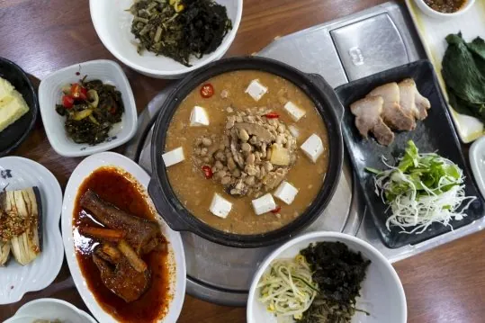 위에서 본 한 상 — 가운데 청국장 뚝배기, 둘레에 고기 접시·생선조림·나물 반찬